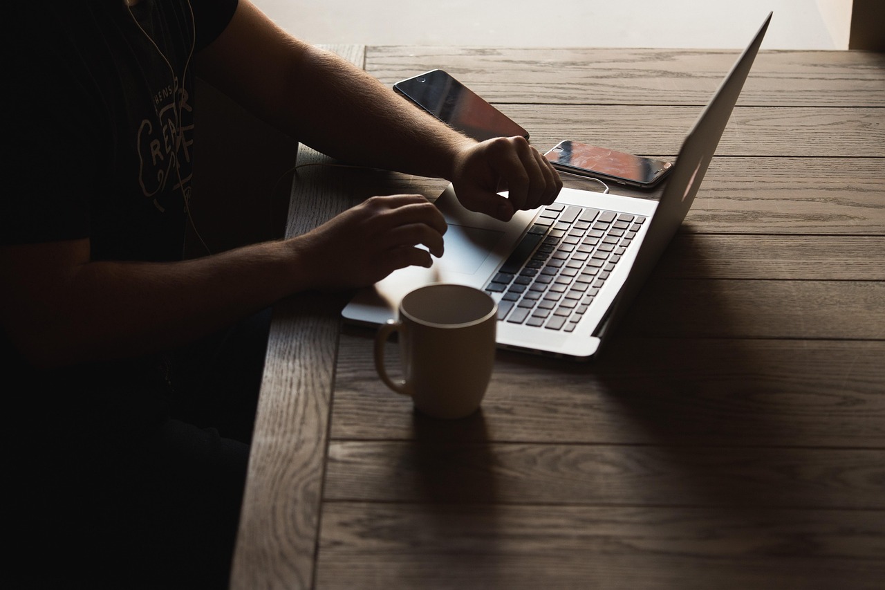 Person using a laptop on wood table next to coffee mug