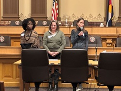Three members of the Colorado Public Health Association in a government building, one speaking into a microphone