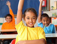 children in classroom with hands raised